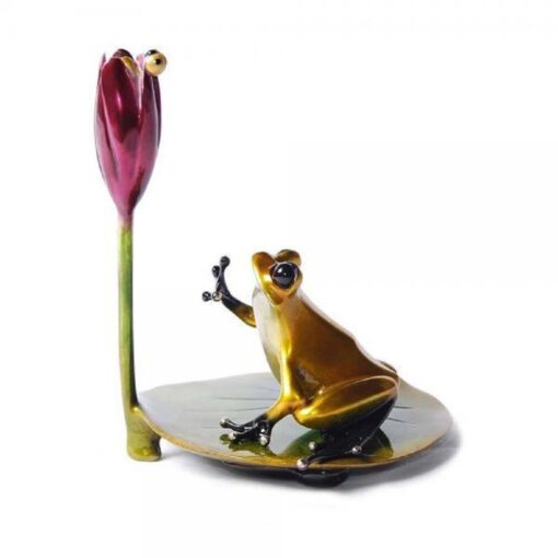 A frog sitting on top of a plate next to a flower.
