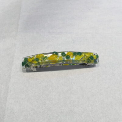 A yellow and green flower barrette on top of white paper.