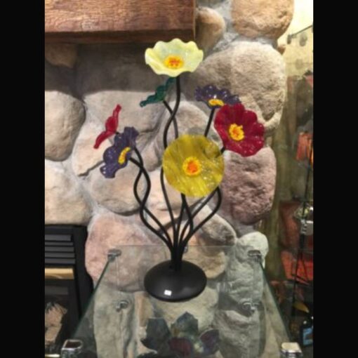 A glass sculpture of flowers on display in front of rocks.