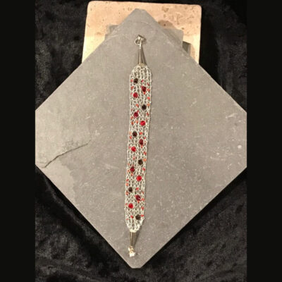 A silver and red bracelet on top of a black tile.