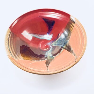 A red bowl with a brown rim and some blue on it