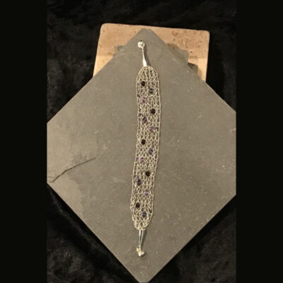 A silver bracelet with purple stones on top of a book.