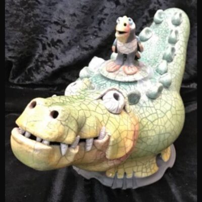 A ceramic alligator with a small figurine on top of it.