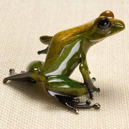 A green and brown frog sitting on top of a white surface.