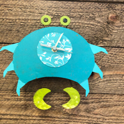 A blue crab clock with yellow hands on top of it.