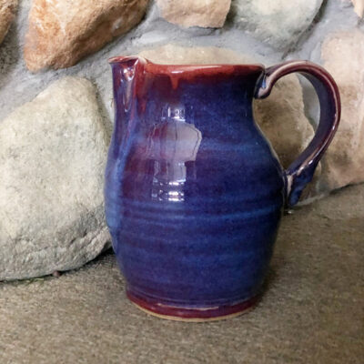 A blue and red pitcher sitting on top of a stone floor.