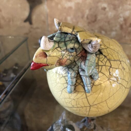A ceramic figurine of an animal sitting on top of a cracked egg.