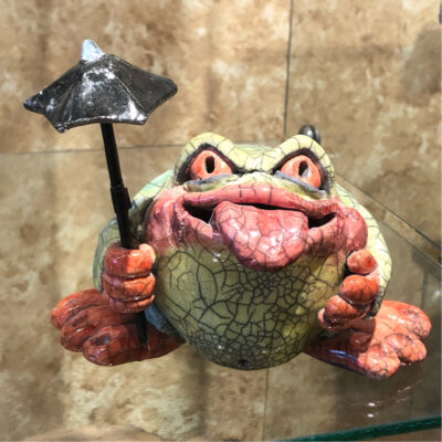 A frog with a umbrella in its mouth.