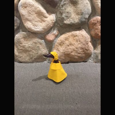 A yellow traffic cone sitting on the ground near some rocks.