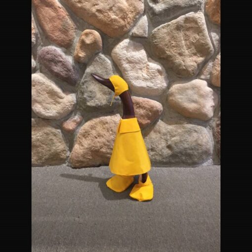 A yellow duck is standing in front of a stone wall.
