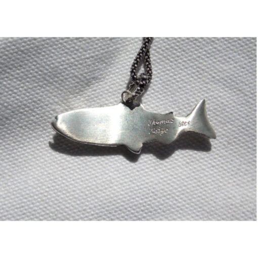 A fish shaped necklace on a white cloth.