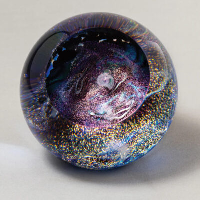 A glass ball with gold and purple swirls on it.