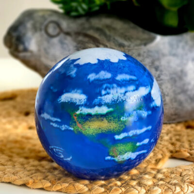 A blue ball with clouds on it sitting next to a plant.